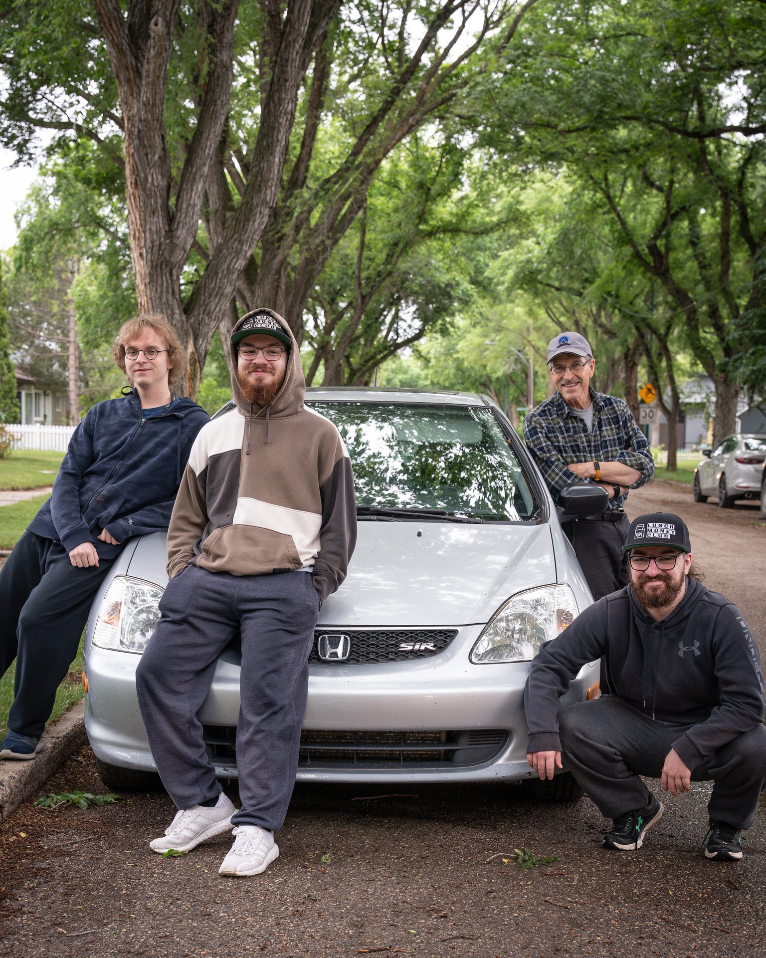 Group of friends posing with a silver Honda Civic on a tree-lined Saskatoon street