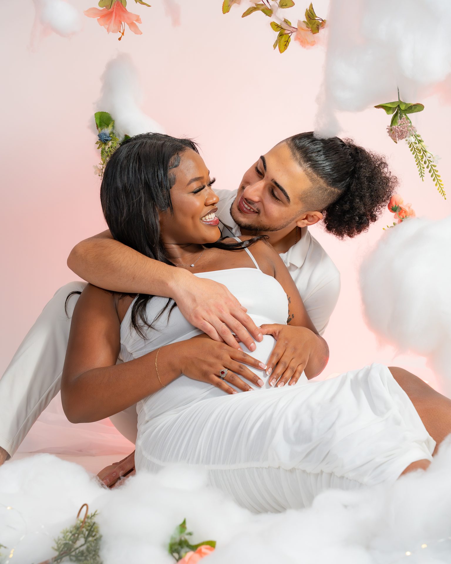 Laughing maternity couple on a pink cloud and flower studio set in Saskatoon