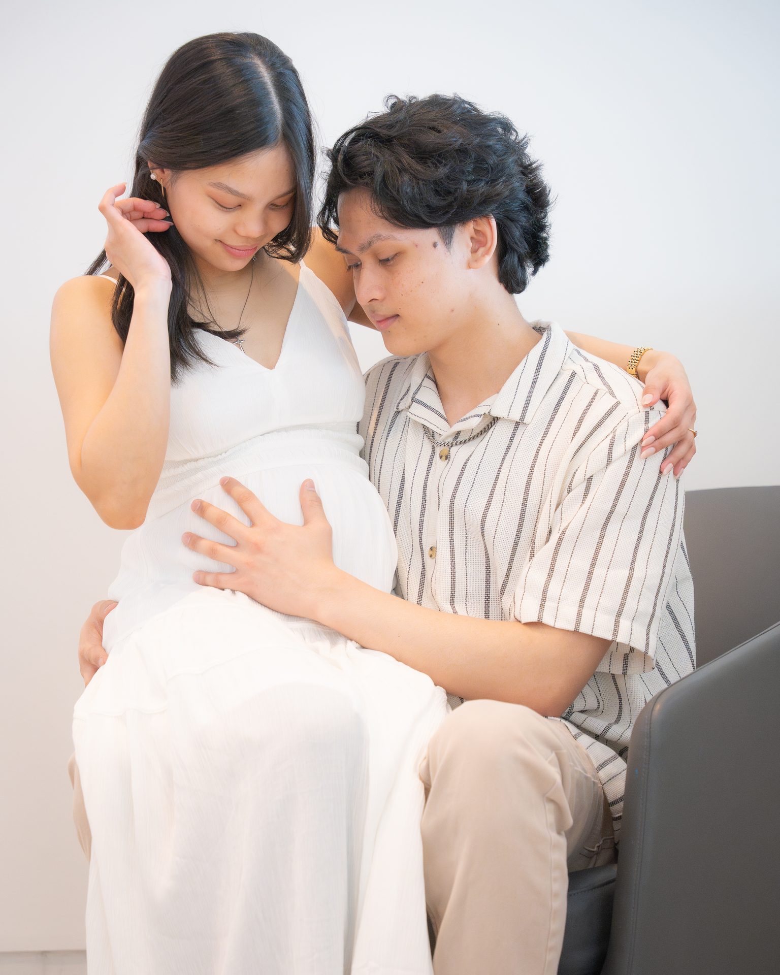 Maternity couple seated together in the studio, hands on the bump